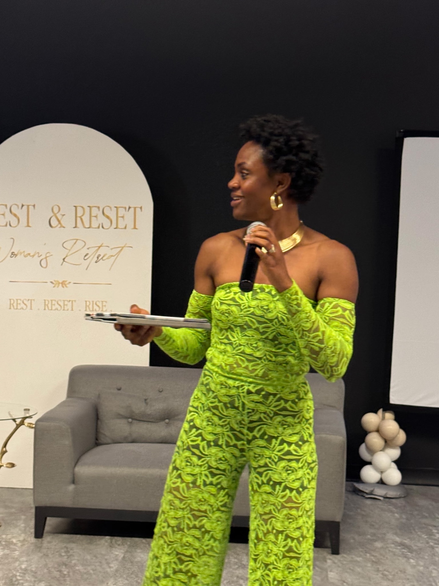Host in a green lace ensemble speaking to guests at the retreat
