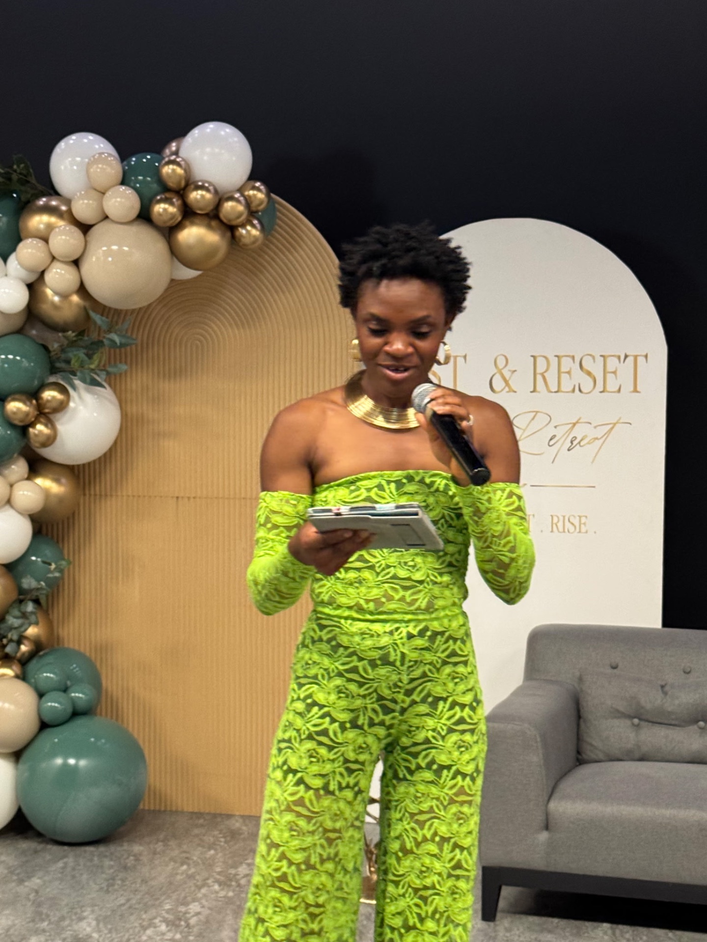 Host reading from her notes beside the balloon garland backdrop